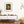 Modern living room with a wooden console table, decorative pillows, and framed sunlit autumn tree artwork.