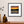 Framed artwork of an orange sunrise over water on a wall above a wooden shelf with decorative items.