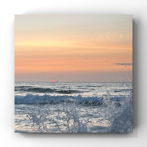 Sunset over the ocean with waves crashing on the shore