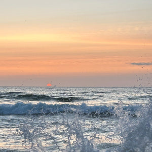 Sunset over the ocean with waves crashing on the shore