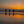 Three people standing on a beach at sunset, silhouetted against the orange sky.