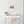 Framed sunset artwork above a white desk with a chair, clock, and flowers.