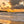 Sunset over a beach reflected in the wet sand with waves crashing onto the shore