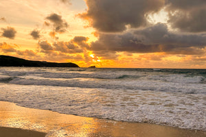 Sunset over a beach reflected in the wet sand with waves crashing onto the shore