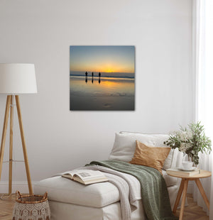 Living room with a painting of three people on a beach at sunset, reflected in wet sand. The room also has a lamp, and a sofa.