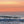 Pale orange and pink sunset with orange sun on the horizon. There is a splash of ocean wave in the foreground