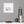 square white frame with an image of a soaring bird above sea cliffs. The picture s on a grey wall with wooden trinkets on a shelf below