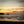Two people walking on a beach at sunset with a silhouetted headland in the background
