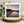 Greetings card of a sunset reflected  in water . Displayed on a wooden stand with a plant and blanket in the background.