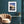 Framed colourful sunrise artwork on a teal wall with a beige armchair and small table below.