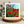 White bordered greetings card of red poppies and blue sky displayed on a wooden stand with a natural background