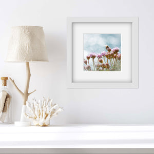 sea pinks flowers with bee print in a square frame on a white wallwith a cream lamp to one side