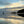 Two people standing on a beach with a reflective water surface and a dramatic sunset sky.