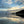Two people standing on a beach with a reflective water surface and a dramatic sky.