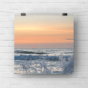 Print of a sunset over the ocean with waves on a white brick wall.