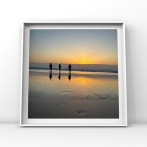 Framed artwork of three people walking on a beach at sunset reflected in the wet sand