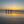 Three people standing on a beach at sunset, with their reflections visible in the wet sand.