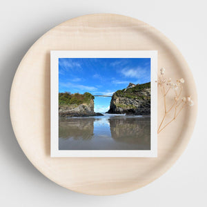 White bordered photograph of a coastal landscape with a clear blue sky on a greetings card displayed on a beige plate.