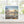 White edged beach sunset print on a greetings card displayed on a wooden surface with a window in the background