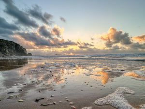 Beach scene with sunset and clouds reflecting on the water