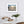 Framed beachscape sunset print reflected on wet sand, on a white wall above a dining table with chairs.