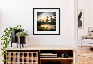 Framed photograph of a sunset over a wooden bridge in a modern living room.