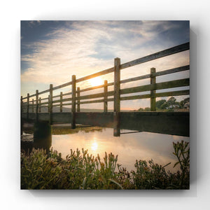 Wooden bridge over water with sunset in the background