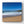 Beach scene with waves crashing onto the shore under a clear blue sky.