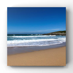 Beach scene with waves crashing onto the shore under a clear blue sky.