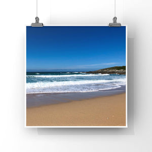 Beach scene with blue sky, ocean waves, and sandy shore.