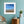 Framed beach print on a teal wall with a wooden side table and plant.