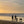 Two people walking with two dogs on a beach at sunset.